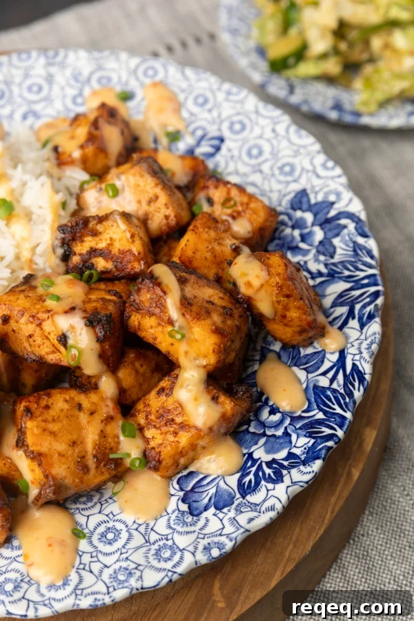 Crispy Bang Bang Salmon Bites Recipe for Spicy Sweet Salmon Bites 3 crispy air fryer bang bang salmon bites drizzled with sauce served with ice on a blue and white floral plate