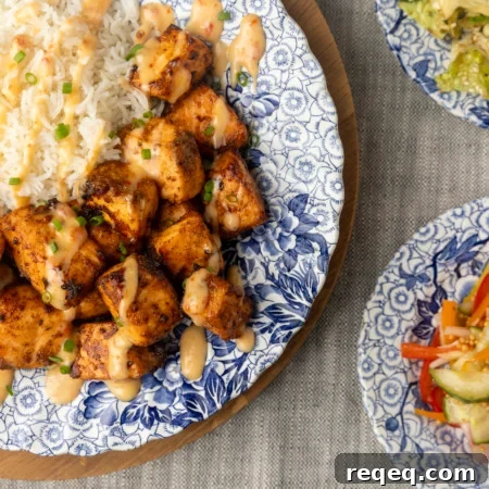 Crispy Bang Bang Salmon Bites Recipe for Spicy Sweet Salmon Bites 7 crispy air fryer bang bang salmon bites drizzled with sauce served with ice on a blue and white floral plate and two smaller blue and white plates with Japanese cabbage salad and pickled pepper salad