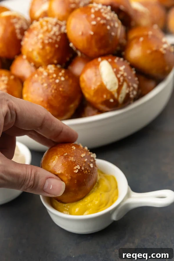 A hand dipping a sourdough discard pretzel bite into mustard.