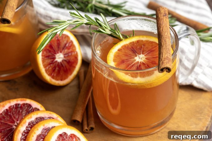 Orange tea in a mug with a slice of orange, a cinnamon stick, and a sprig of rosemary.