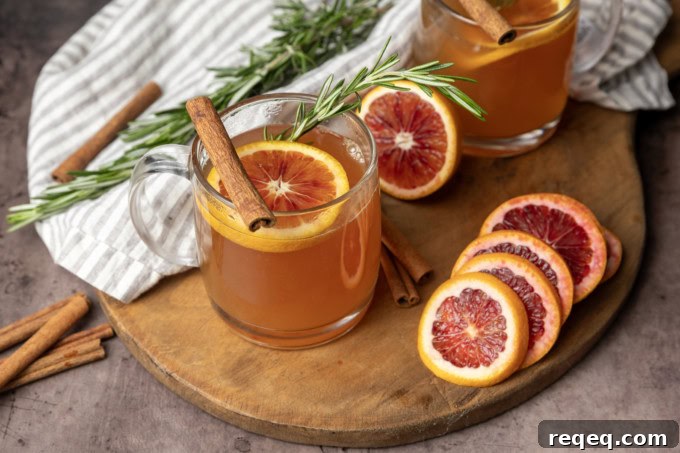Orange tea in a mug with a slice of orange, a cinnamon stick, and a sprig of rosemary.