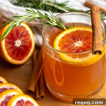 Orange tea in a mug with a slice of orange, a cinnamon stick, and a sprig of rosemary.