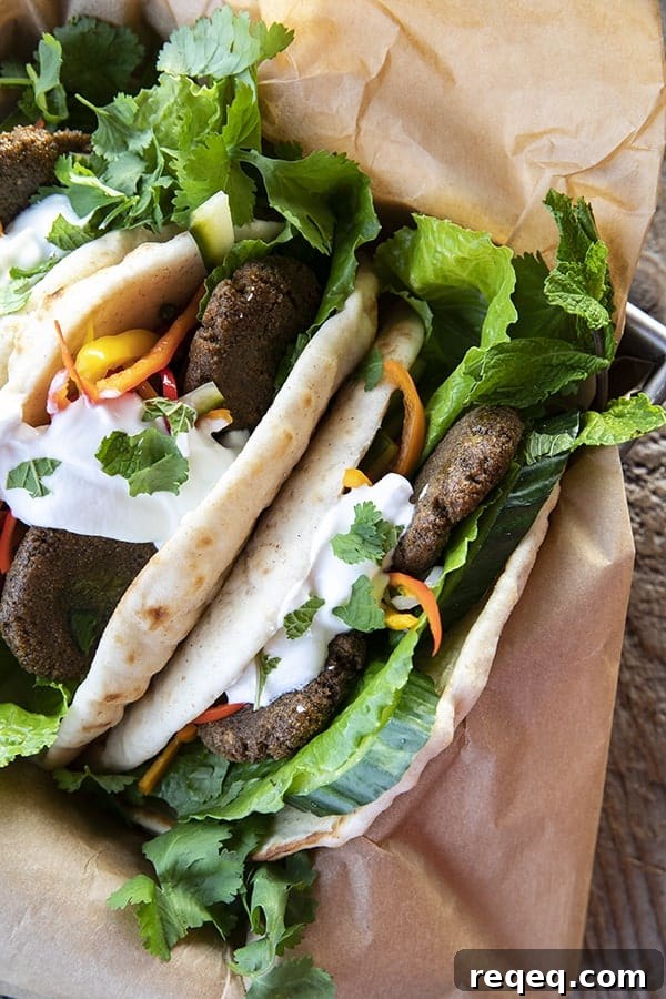 Top view of falafel in flatbread with pickled vegetables, lettuce, yogurt, cilantro, on brown paper.
